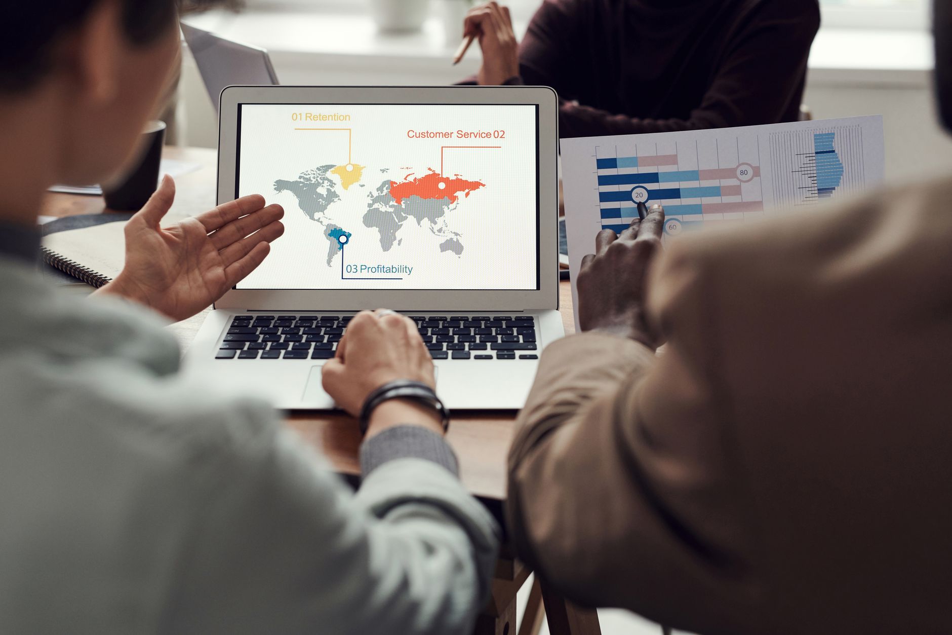 Des collègues discutent autour d’un ordinateur portable affichant une carte du monde et d’un document imprimé avec des graphiques.